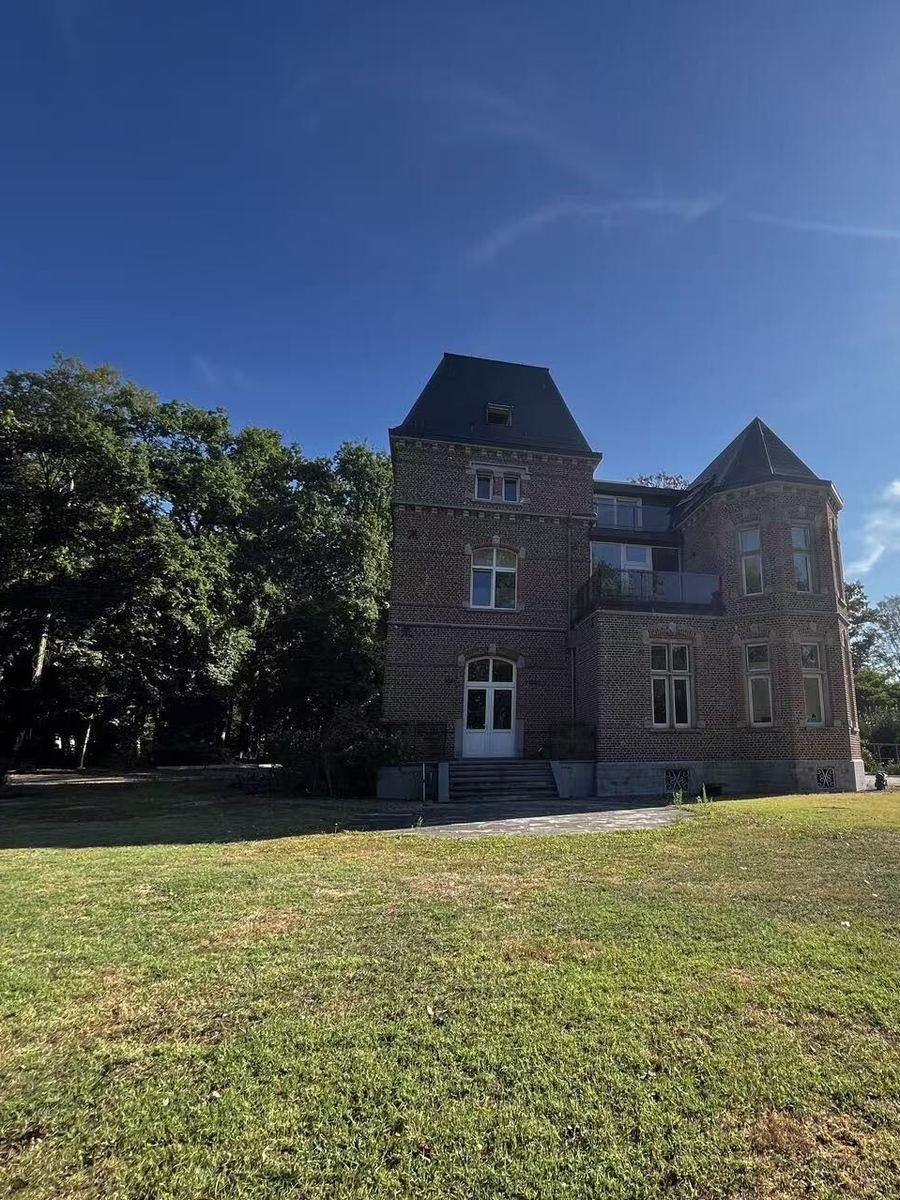 The rear elevation of Clinique de la Brisée in bright sunshine, with a corner turret, first-floor balcony and a wide lawn in front of it.