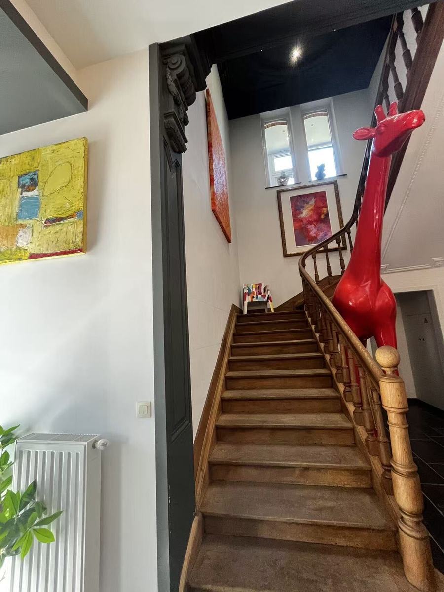 The clinic's original wooden staircase under a black-painted ceiling, with a life-size glossy red giraffe sculpture standing beside the banister and abstract paintings on the walls.