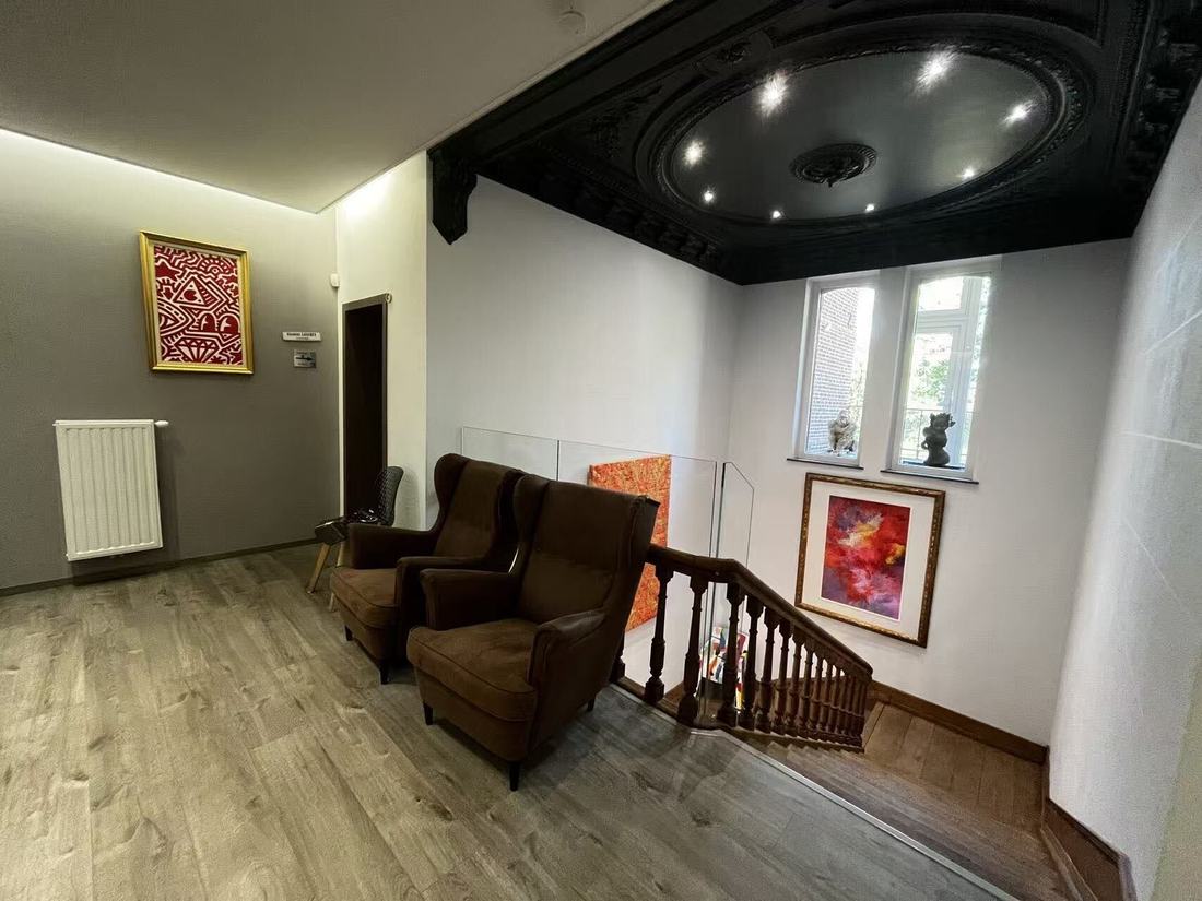 A first-floor waiting area with two brown velvet wing armchairs, a wooden floor and an ornate black-painted ceiling rosette lit by recessed spotlights.